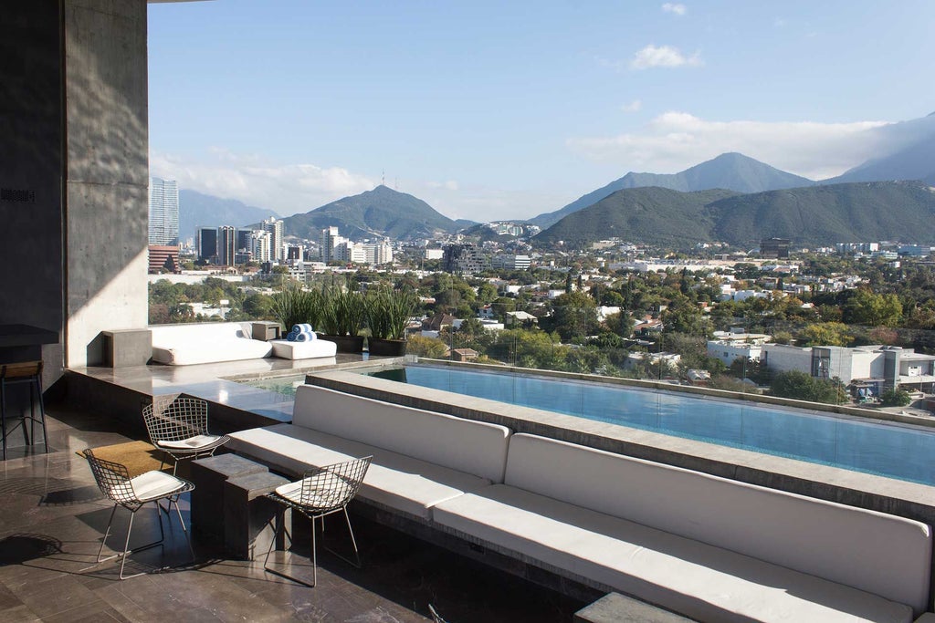 Sleek modernist hotel with glass facade and geometric design, overlooking urban Monterrey skyline, illuminated at dusk with minimalist architectural elegance