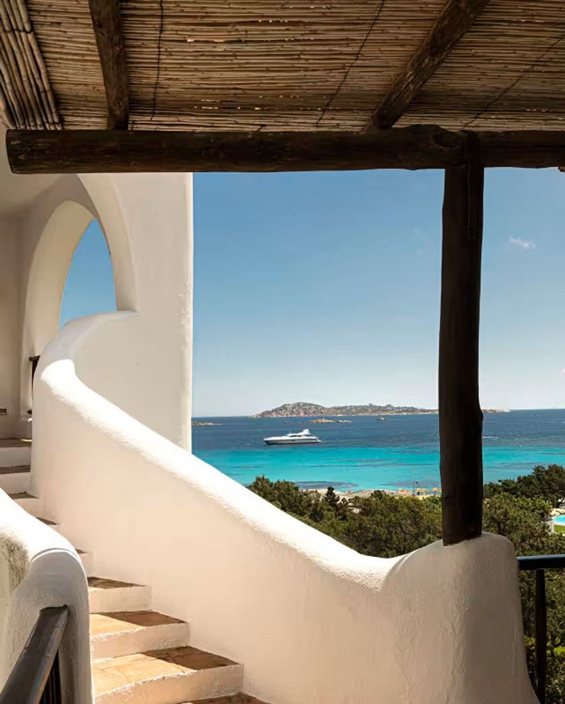 Luxurious Mediterranean villa with white-washed walls, arched windows and terracotta roof overlooking turquoise Costa Smeralda waters