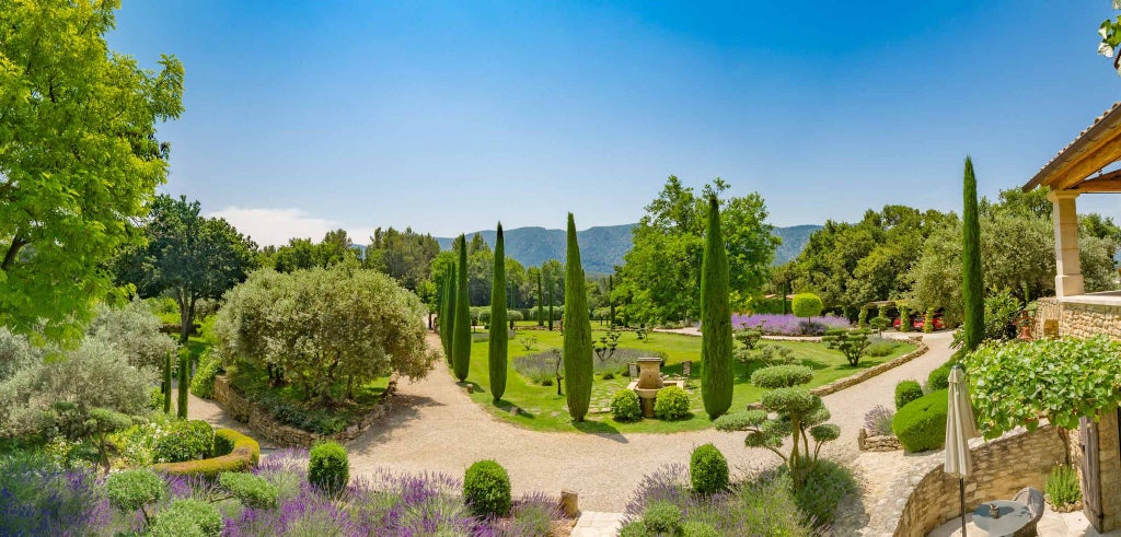 Luxurious French countryside estate with stone farmhouse, manicured lavender fields, and rustic stone terrace overlooking scenic Provence landscape at sunset