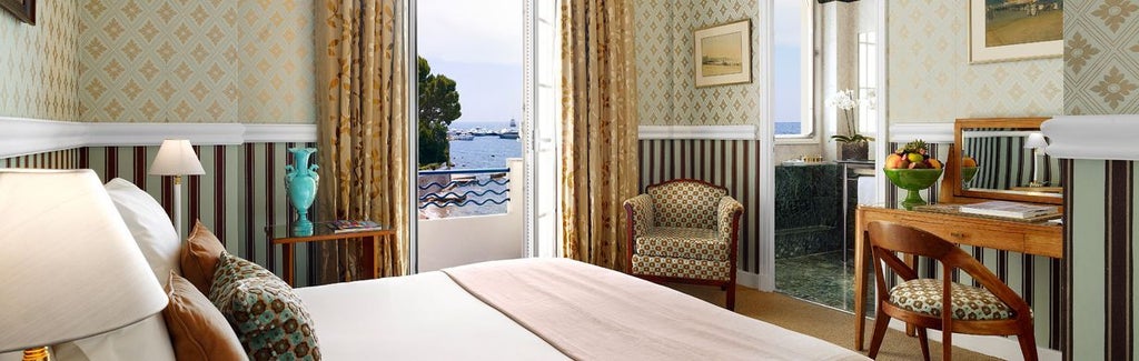 Elegant hotel room with panoramic Mediterranean views, featuring Art Deco furnishings, a marble bathroom, and a private balcony