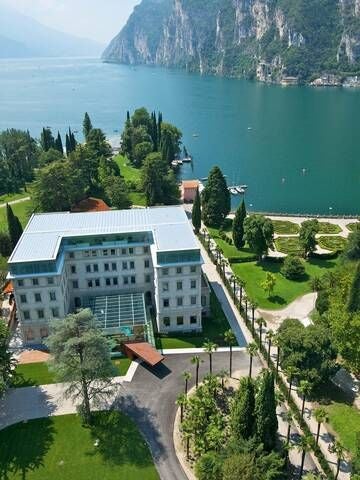 Elegant Art Nouveau hotel facade with ornate white exterior, grand windows, and lush lakeside gardens nestled in scenic Italian landscape