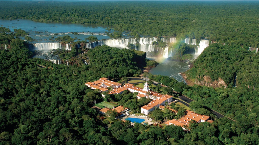 Pink-hued colonial hotel building with ornate facades and manicured gardens nestled beside Iguazu Falls, framed by lush rainforest