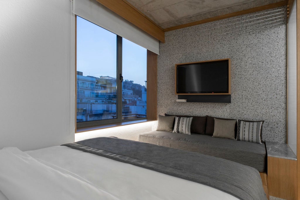 Minimalist luxe hotel room with high ceilings, warm wood accents, neutral linens, and large windows overlooking urban Athens architectural landscape