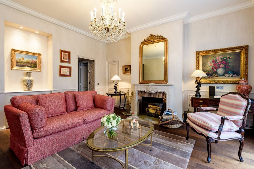 Opulent French hotel room with crystal chandelier, fireplace, and period furniture against cream walls, featuring silk drapes and antique art