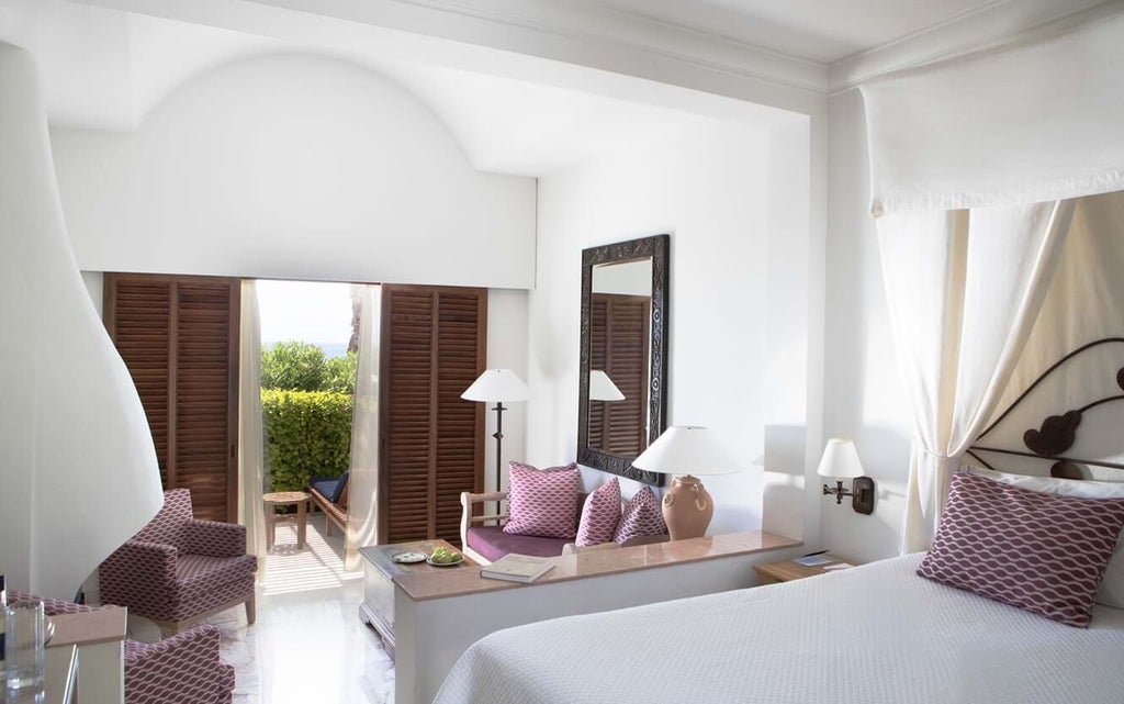 Elegant garden studio suite with modern furnishings, plush white bedding, and sliding glass doors overlooking lush tropical greenery at scenset hotel in Cyprus.