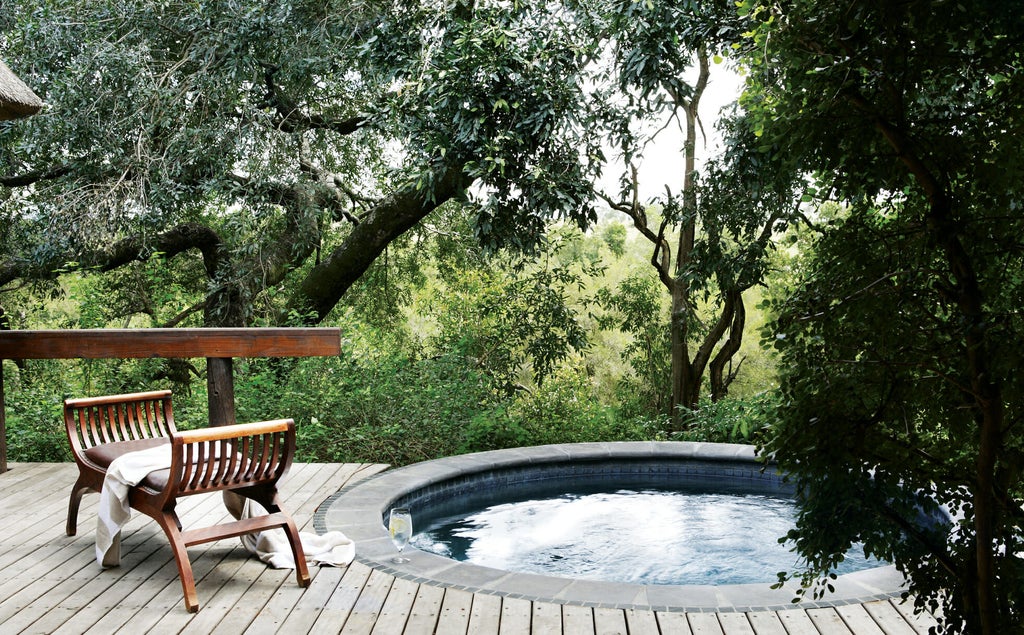 Luxury safari lodge suite with private plunge pool overlooking lush African bush, featuring thatched roof and wooden deck terrace