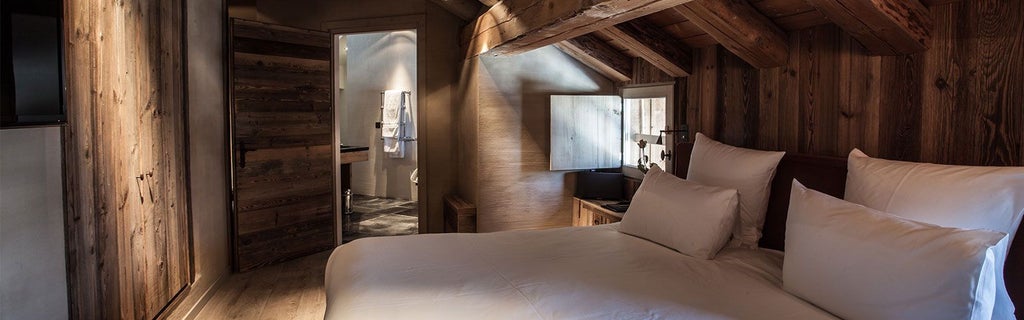 Luxurious alpine-style deluxe room with warm wooden paneling, plush bedding, and panoramic mountain views in French ski chalet setting