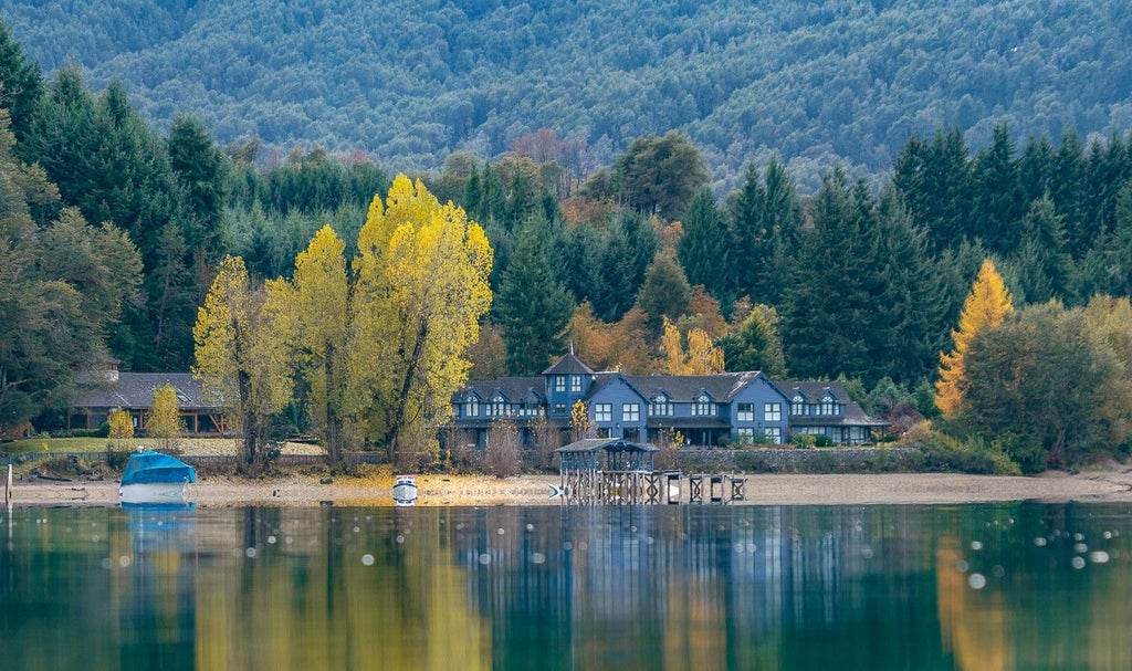 Luxurious lakeside resort with stone and wood facade nestled between Patagonian mountains, reflecting perfectly in calm blue waters