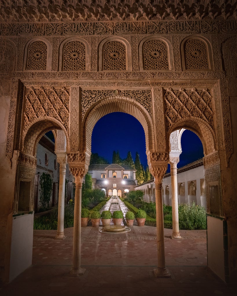 Moonlit Alhambra palace illuminated, golden Islamic architecture glowing against midnight blue sky, intricate stone arches casting elegant shadows