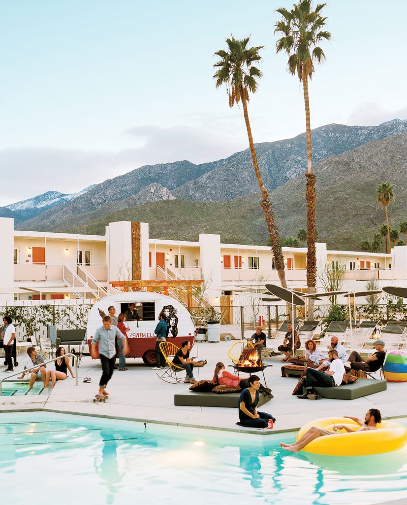 Elegant mid-century modern swimming pool surrounded by palm trees and lounge chairs at Ace Hotel, with mountains rising in the background