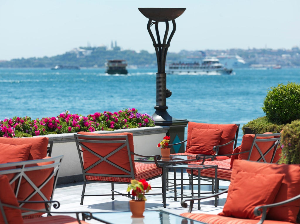 Historic waterfront palace hotel with ornate white facade, elegant arched windows and palm trees overlooking the Bosphorus strait in Istanbul