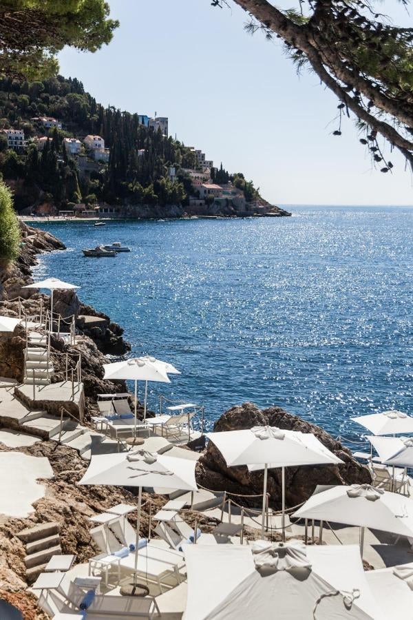 Modern minimalist hotel built into rocky cliffs overlooking Adriatic Sea, featuring glass balconies and private beach access at sunset