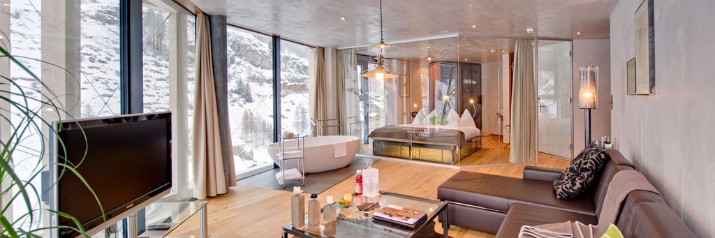 Contemporary alpine hotel with angular glass facade reflecting snow-capped Matterhorn mountain, illuminated at dusk in Zermatt