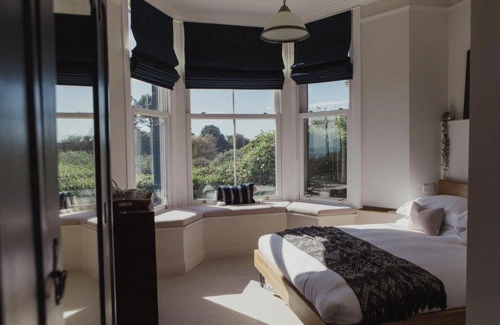 Elegant beige and white hotel room with plush king bed, modern minimalist decor, soft textured throw, city view window in boutique Sandy Duck accommodation