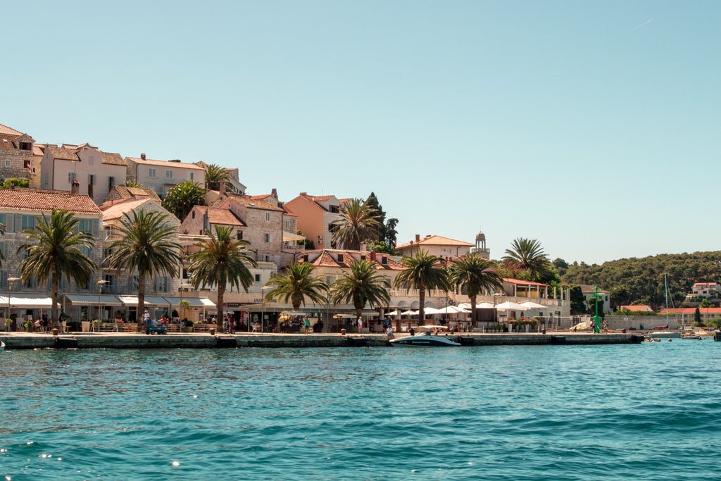 Sleek white speedboat anchored in crystal-clear turquoise waters near Hvar's coastline, with lush Pakleni Islands in the background