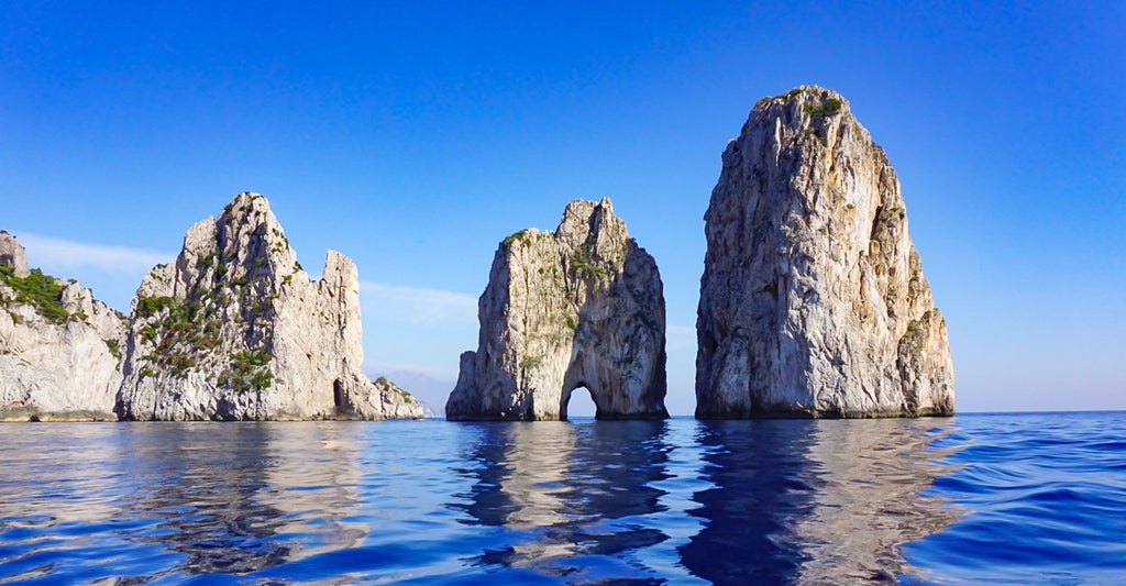 Crystal-clear turquoise waters surround Capri's dramatic limestone cliffs, with luxury yachts anchored near the iconic Faraglioni rock formations