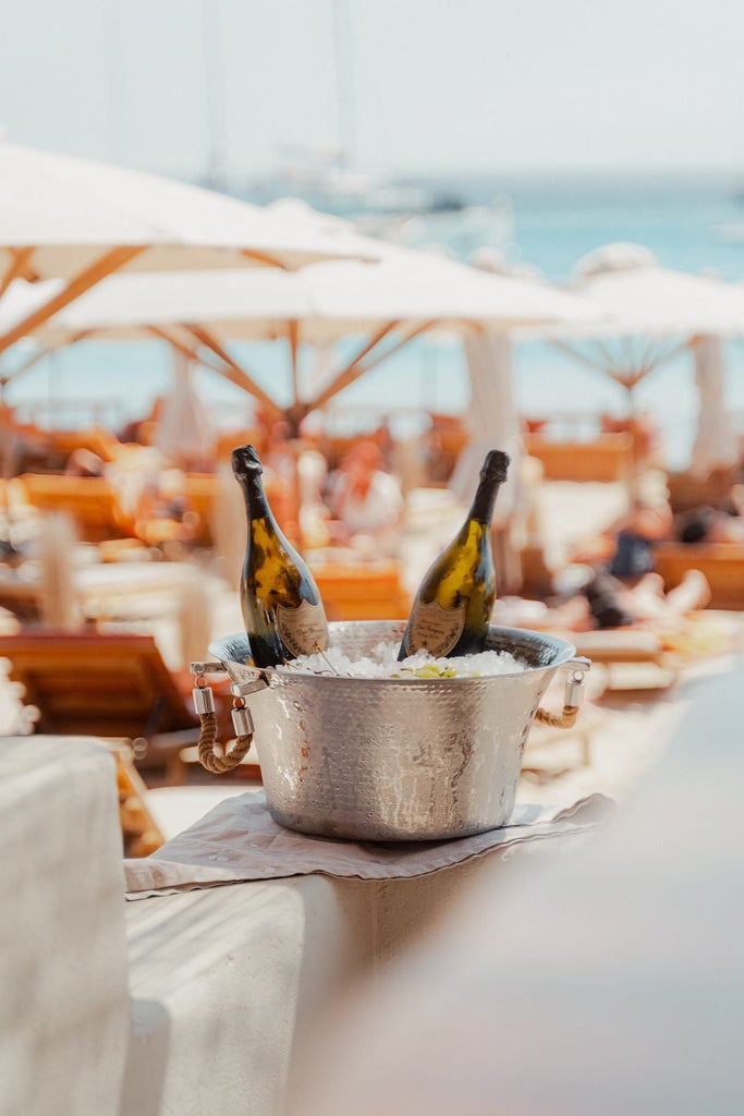 Luxurious white-washed Cycladic hotel perched on a cliff in Mykonos, overlooking the sparkling blue Aegean Sea with minimalist architecture and elegant design