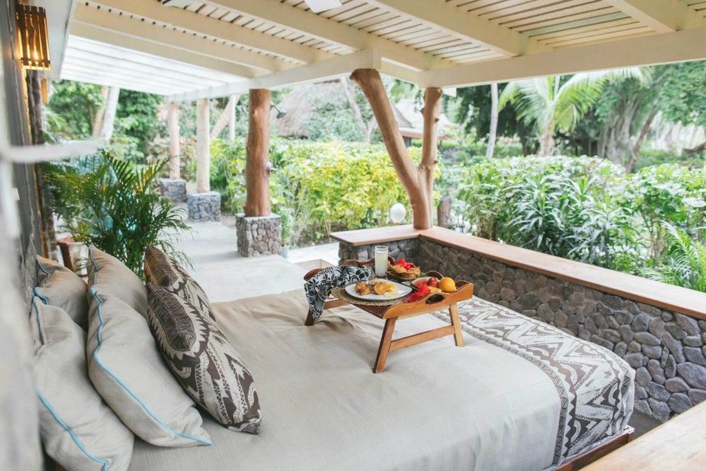 Spacious Fijian beachfront villa with elegant wooden interiors, expansive ocean views, plush king bed, and private balcony overlooking turquoise waters at sunset