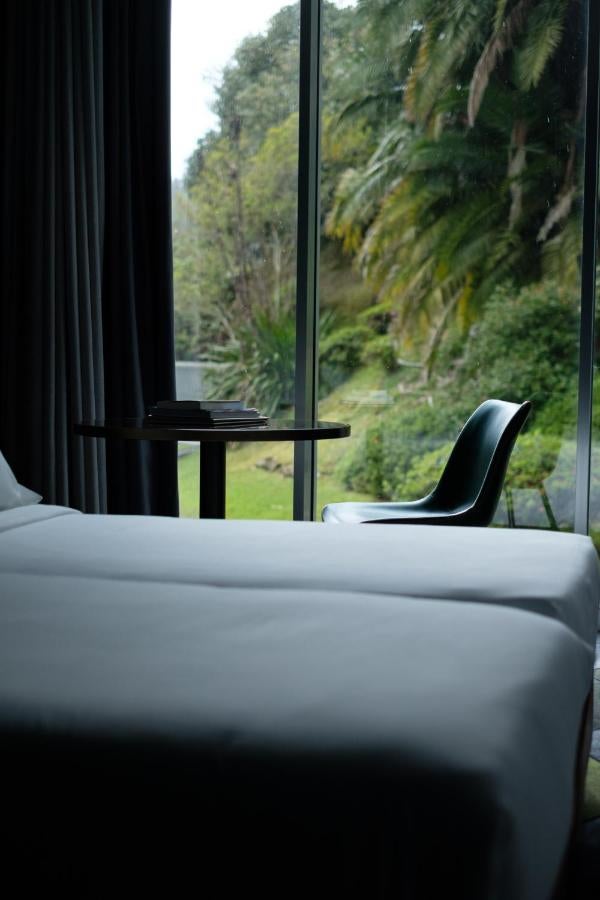 Modern boutique hotel nestled in lush Azorean gardens, featuring elegant white facade, floor-to-ceiling windows and private balconies