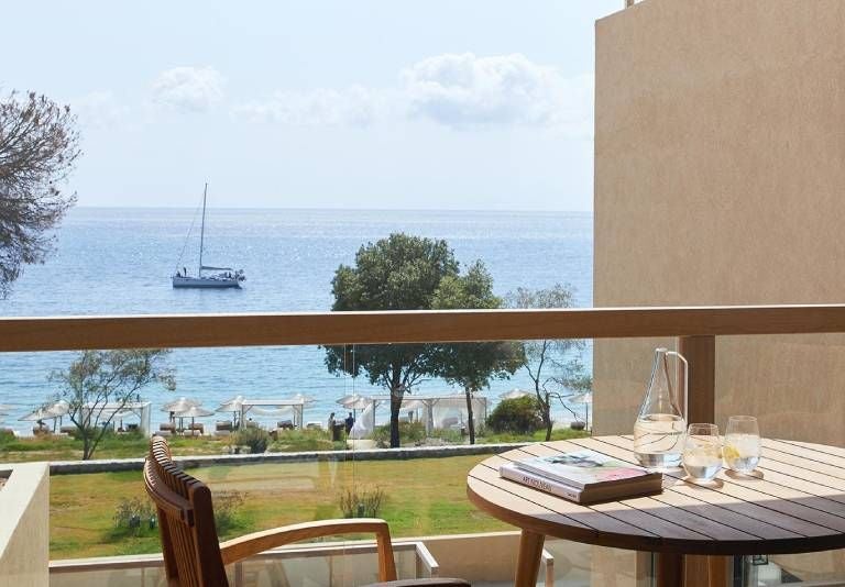 Luxurious double supreme deluxe hotel room at ELIVI Skiathos, featuring elegant white decor, plush bedding, and scenic Greek island views through large windows.