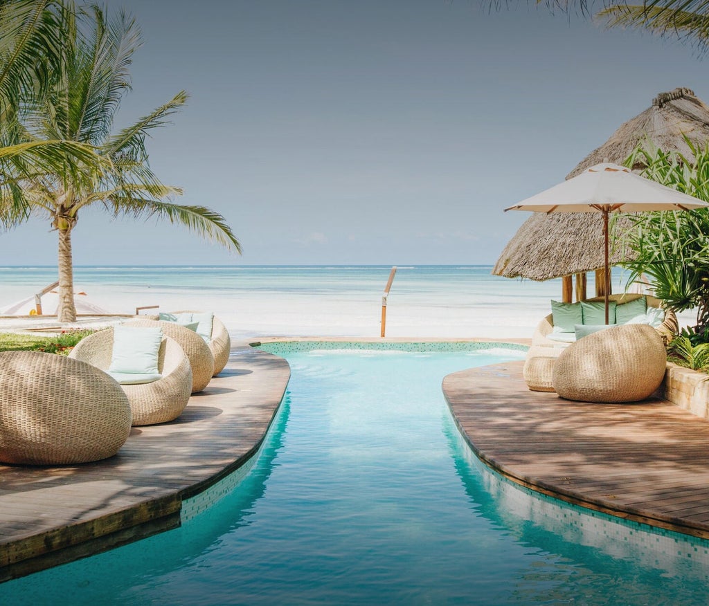 Luxury infinity pool overlooking white sandy beach, with thatched-roof villas nestled among palm trees at Tulia Zanzibar resort