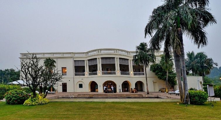 Grand colonial-style Taj Nadesar Palace hotel in Varanasi features white facade, manicured gardens, and ornate architecture against blue sky