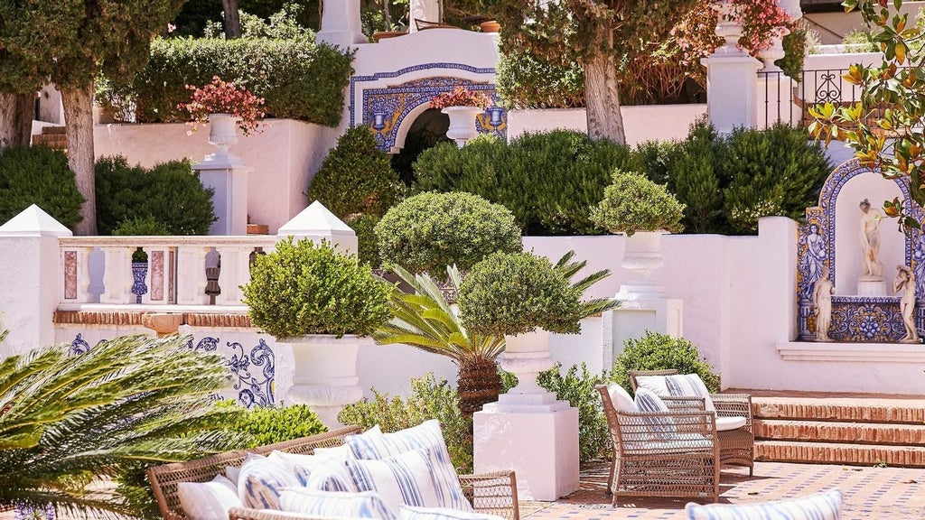 Luxurious Mediterranean hotel with white-washed buildings, lush tropical gardens, and sparkling blue pool overlooking the scenic coastal landscape of scenset Spain.