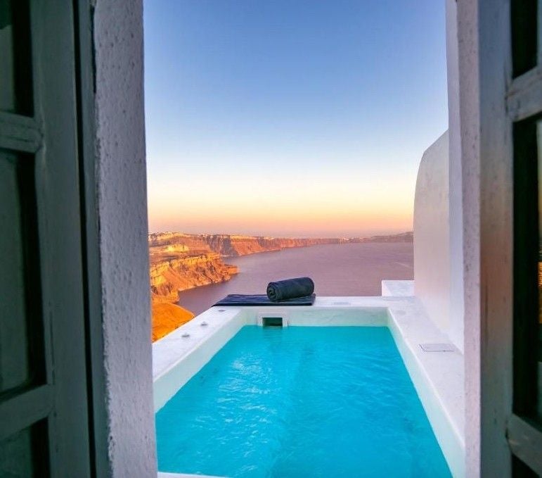 Elegant white-washed Greek hotel with private infinity pools overlooking the Aegean Sea, set against dramatic coastal cliffs at sunset