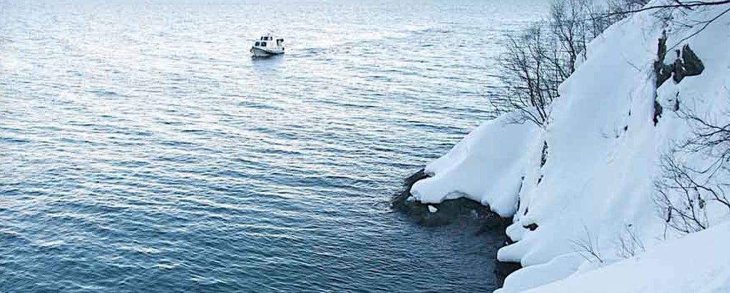 Luxury sea safari boat cruising through pristine Norwegian fjords, surrounded by dramatic snow-capped mountains and crystal-clear arctic waters