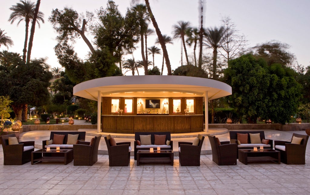 Elegant colonial-era hotel with white facade, ornate balconies and palm trees along Luxor's Nile River promenade at sunset