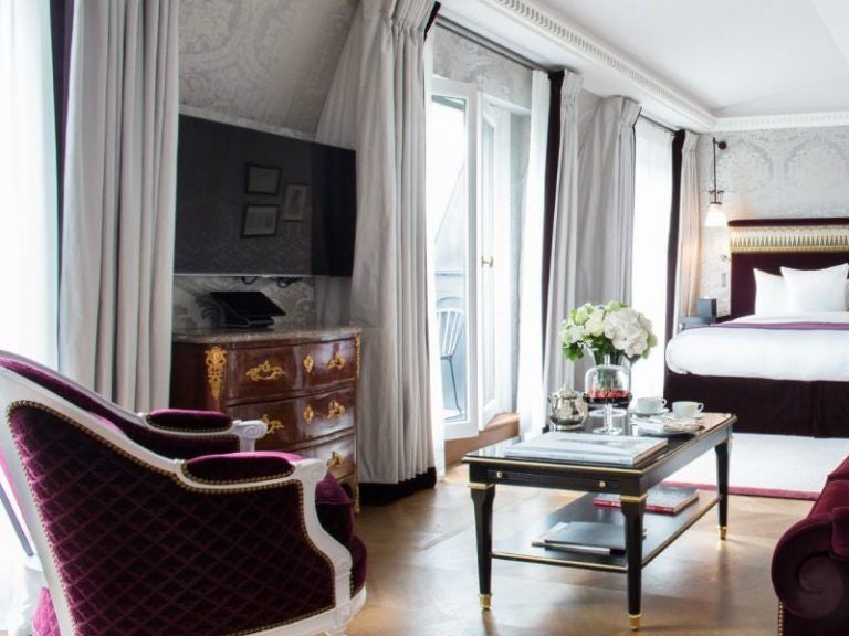 Opulent Parisian suite featuring antique furnishings, crystal chandelier, plush seating, ornate gold-framed mirrors, and balcony views of the city