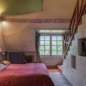 Elegant French château room with ornate four-poster bed, antique furnishings, and soft natural light filtering through large period windows