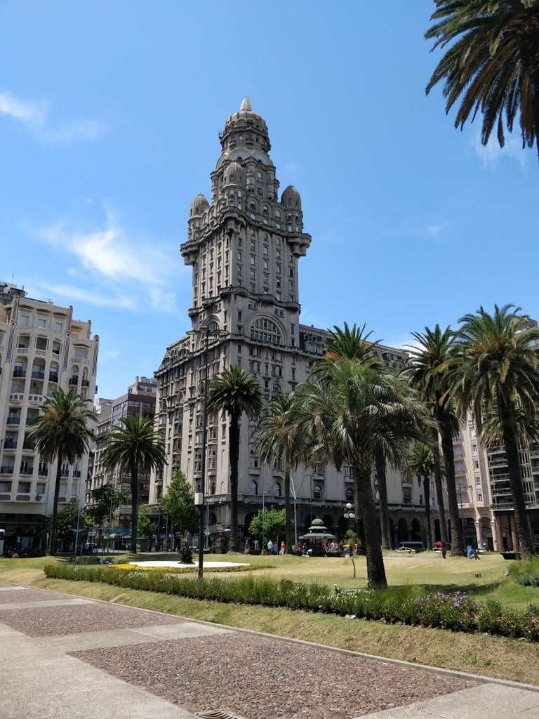 Colonial-style luxury hotel in heart of Montevideo at sunset, warm lights illuminating ornate white stone facade with palm trees lining entrance