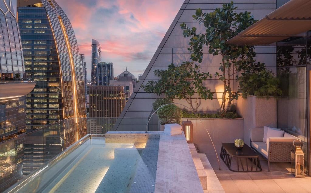 Modern triangular glass skyscraper of Rosewood Bangkok hotel rises dramatically against city skyline, reflecting golden sunset light