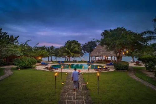 Lush tropical garden surrounding elegant white colonial-style villa with palm trees, vibrant flowers, and a serene outdoor seating area in Argentina.