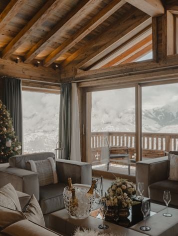 Luxurious alpine hotel room with elegant wooden accents, plush white bedding, and large windows overlooking snow-capped mountain scenery in Courchevel, France