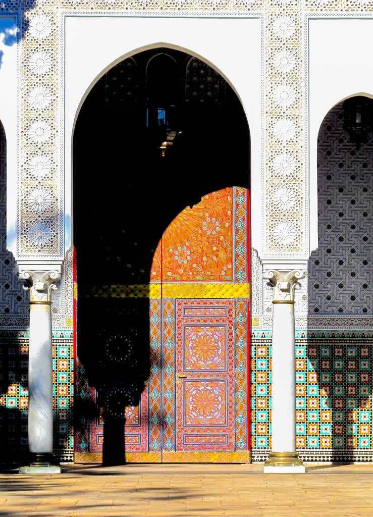 Whitewashed Moroccan archway adorned with ornate blue-tiled mosaics and brass lanterns, framing a luxurious courtyard entrance