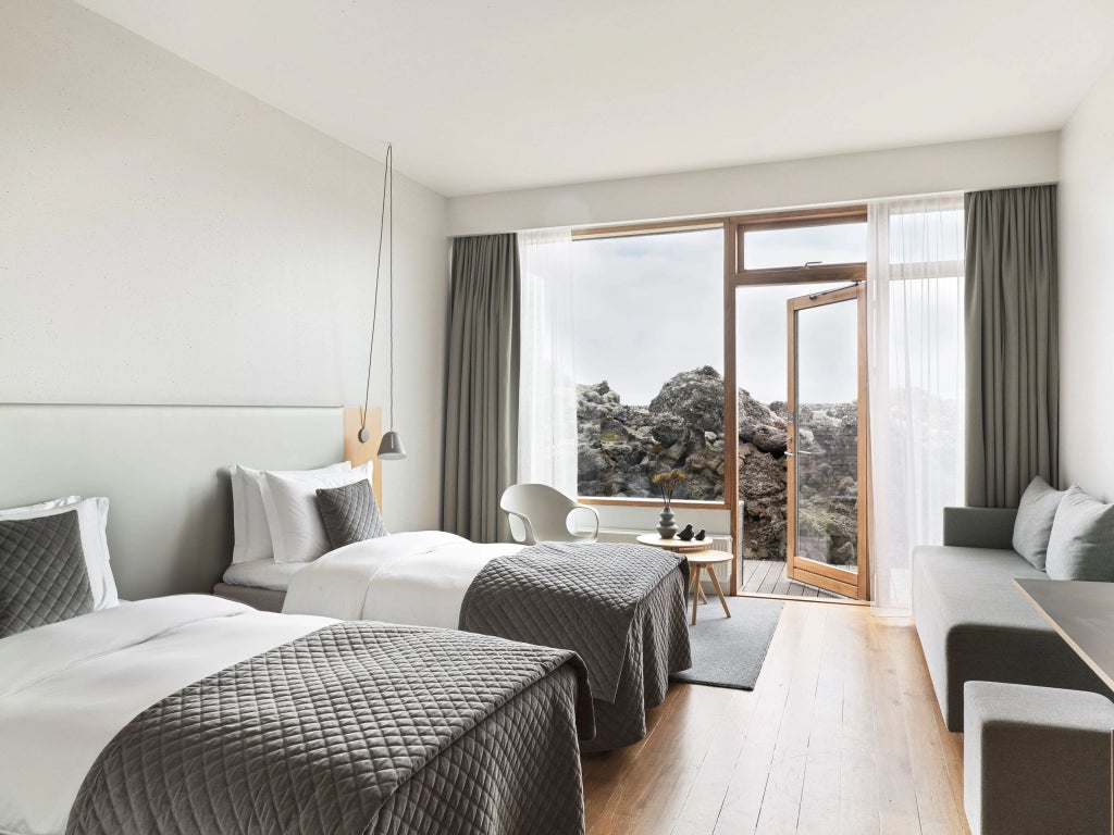 Minimalist Icelandic hotel room with panoramic windows, sleek Nordic design, volcanic stone accents, and serene blue-gray color palette showcasing modern luxury.