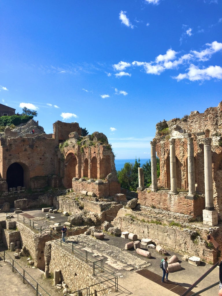 Historic coastal town Taormina cascading down Sicily's cliffs, with golden stone buildings and the Mediterranean Sea sparkling below