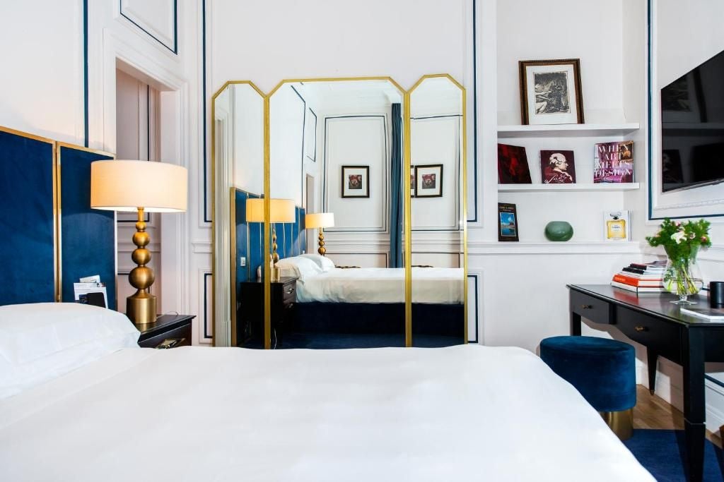 Elegant marble-clad Dama Suite at Palazzo Dama, featuring plush white bedding, contemporary design, and soft natural lighting in a luxurious Roman setting