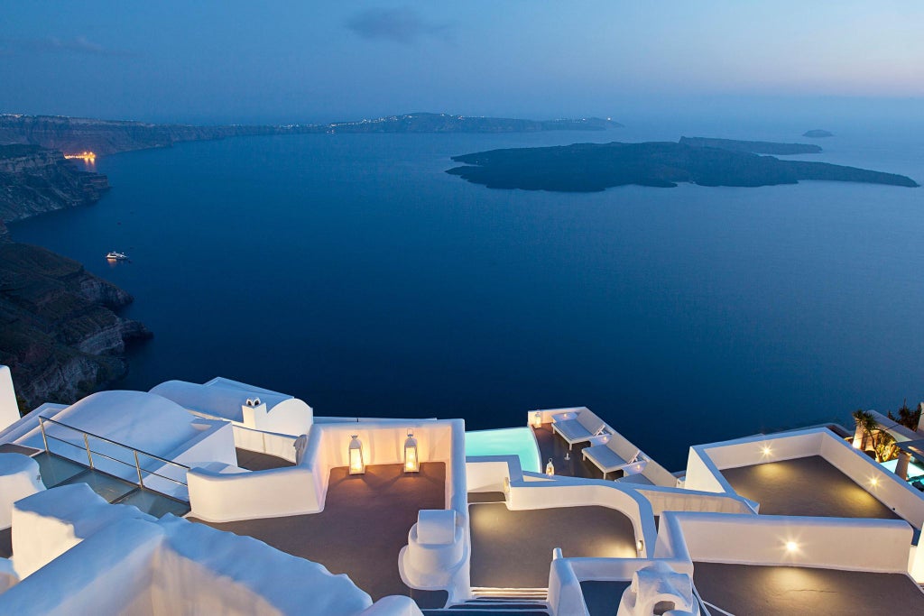 Elegant white-washed luxury resort with infinity pools cascading down Santorini's cliff, overlooking azure Aegean Sea with pristine architectural design