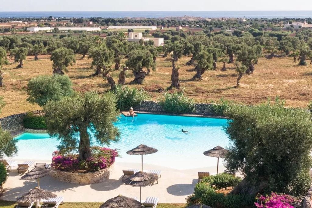 Ancient stone masseria hotel in Puglia with whitewashed walls, arched windows and flowering Mediterranean gardens set against blue sky