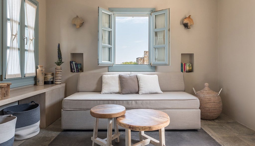 Minimalist white bedroom with panoramic Aegean Sea view, clean lines, elegant furnishings, and a private balcony overlooking scenic Greek island landscape at sunset