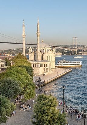 Elegant five-story boutique hotel overlooking Bosphorus Strait, featuring modern white facade, blue waters, and Istanbul's historic skyline in background