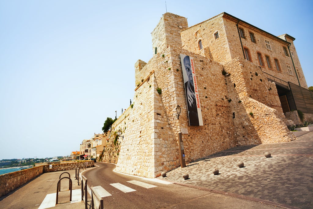 Sunlit medieval village of Saint-Paul-de-Vence perched on hilltop, with stone walls, cobblestone streets and distant French Riviera views