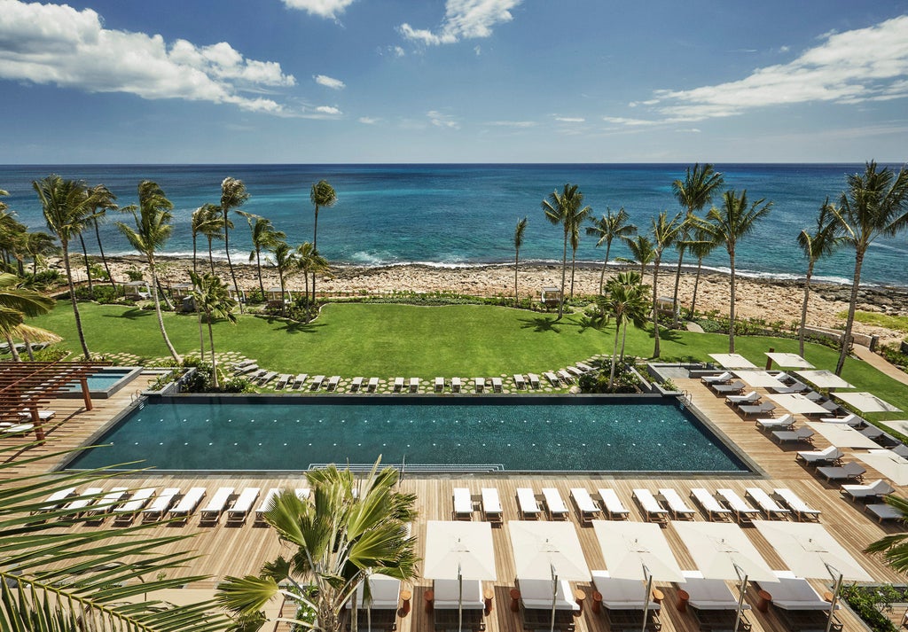 Luxurious oceanfront resort with infinity pools cascading toward pristine beach, surrounded by swaying palm trees and tropical gardens