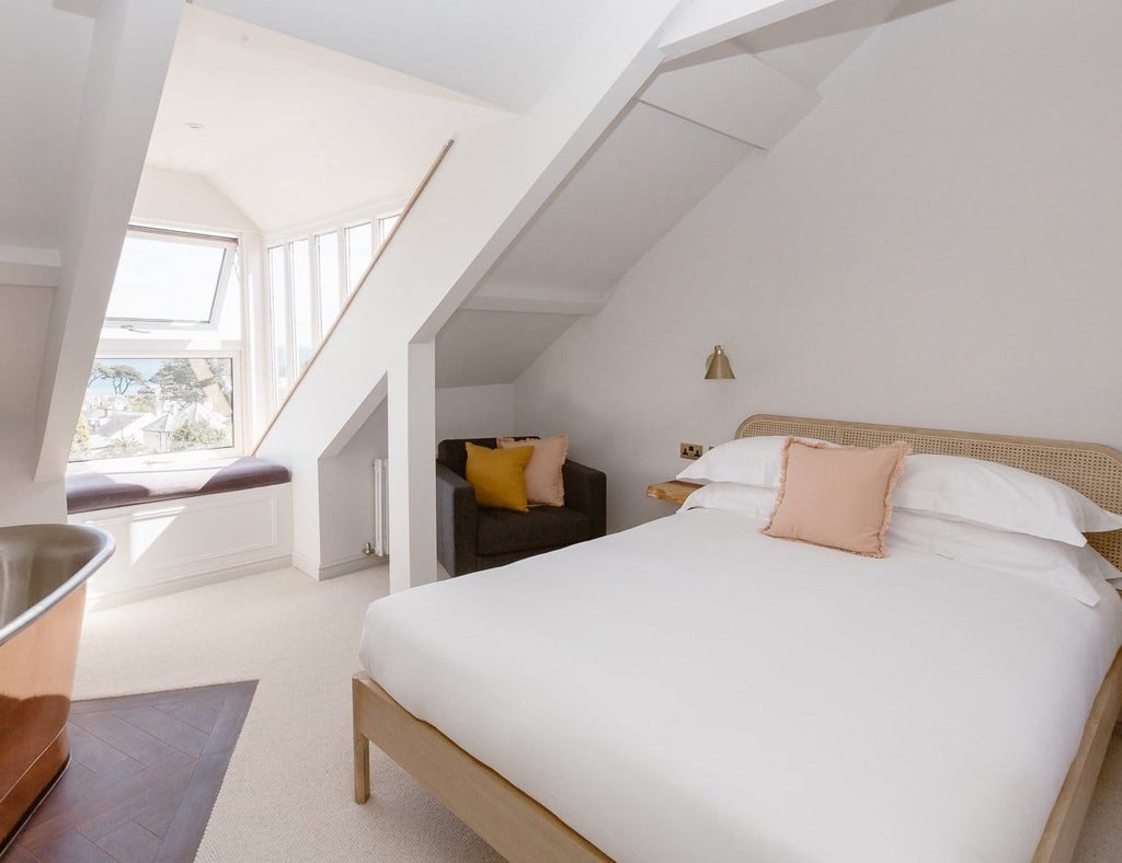 Spacious coastal-style bedroom with plush white bedding, seaside-inspired decor, warm wooden furnishings, and soft natural lighting in a luxurious UK hotel room