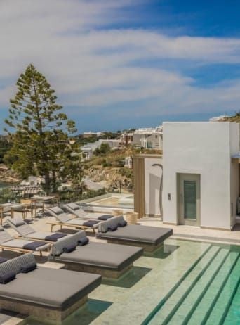 Luxurious white-washed Cycladic hotel with blue accents overlooking Aegean Sea, featuring minimalist design and infinity pool at sunset in Mykonos