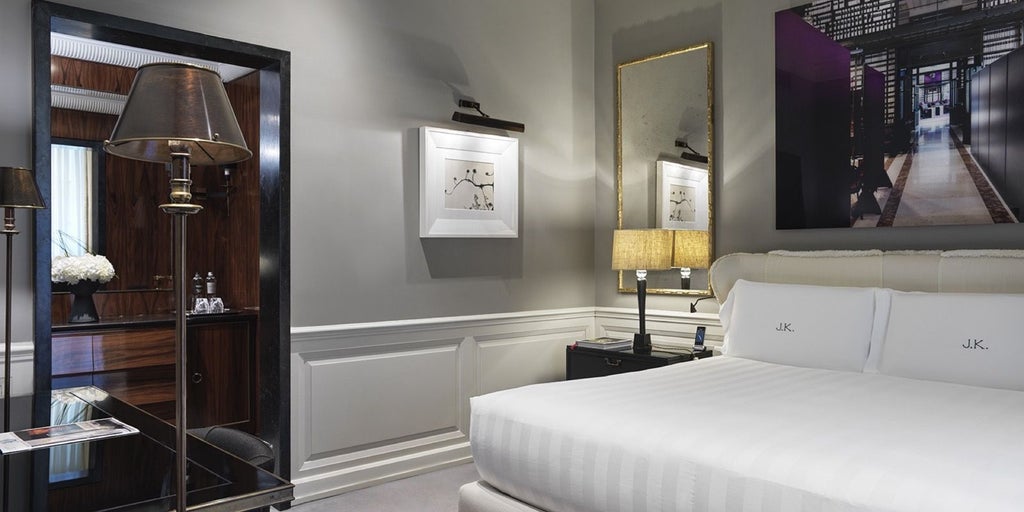 Elegant deluxe hotel room with soft neutral tones, luxurious king bed, marble bathroom, and chic Italian design in a refined Roma setting