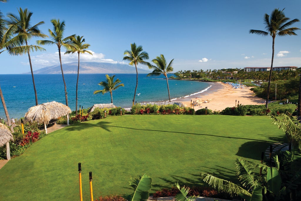 Luxury oceanfront resort with infinity pool overlooking white sandy beach, palm trees and Pacific Ocean at sunset in Maui, Hawaii